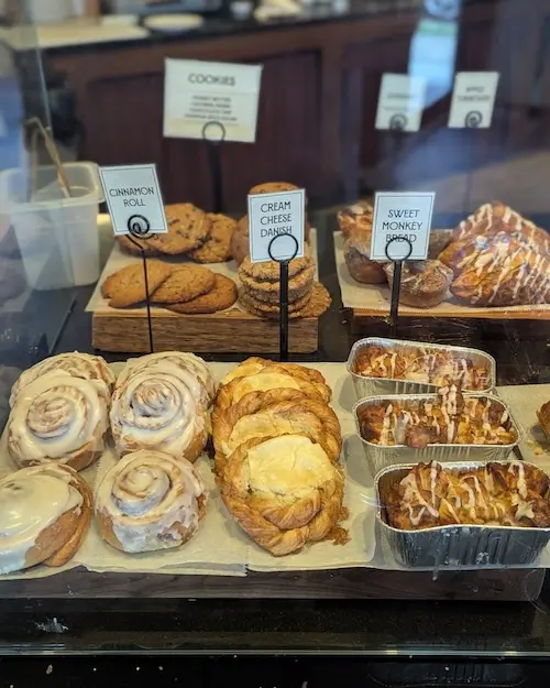 Danish and pastry display with cinnamon rolls, cream cheese danish, sweet monkey bread, and other cookies and pastries in the background.